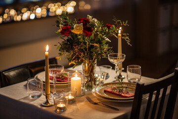 holidays, romantic date and celebration concept - close up of festive table serving for two with flowers in vase and candles burning at home on valentine's day