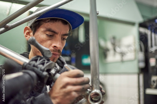 Hispanic man removing paint residue from a bicycle frame as part of the process of a bike renovation work made at his workshop.
