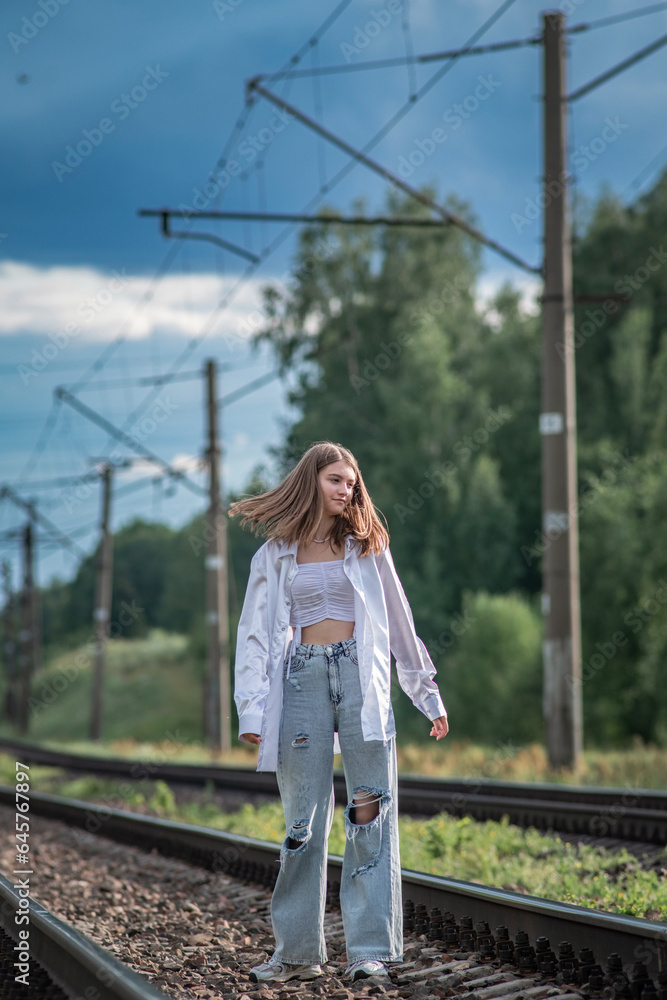 A young beautiful long-haired girl in jeans and a shirt stands on the railway tracks. A young beautiful long-haired girl in jeans and a shirt stands on the railway tracks.