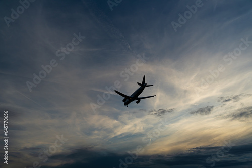 Silhouette of an airplane against the cloudy sky in the fading evening light