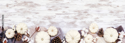 Cozy autumn bottom border with blanket  white pumpkins natural decor. Top down view over a white wood banner background. Black  white and brown theme.