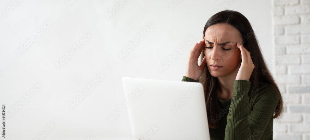 Close up portrait of a young brunette tired woman, who is sitting with her eyes closed, touching her head while suffering from a migraine or headache Close up portrait of a young brunette tired woman, who is sitting with her eyes closed, touching her head while suffering from a migraine or headache