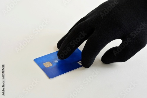  A hand in a black glove steals a bank card . The concept of stealing money from bank cards.