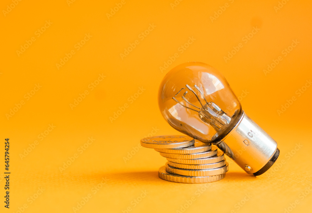 A lamp and money on a orange
 background with copy space. Price for electricity concept. Expensive electricity cost. - obrazy, fototapety, plakaty 