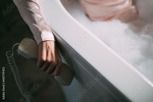A young woman in a dress is lying in a bubble bath with a phone handset in her hand. Conceptual photo.