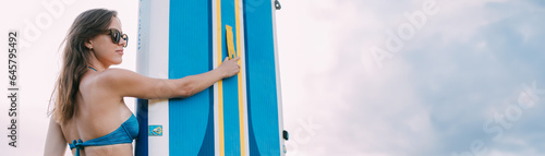 A young woman with an open swimsuit stands with a sapboard on the shore of the lake. Stand Up Paddle. SUP touring photo