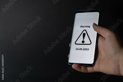 Symbol for the national warning day in Germany, 2022. Hand holds a mobile phone with the German text 