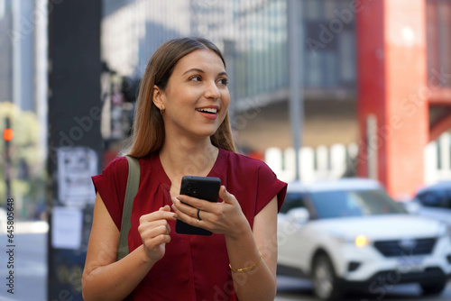Close-up of attractive Brazilian business woman hail a vehicle using mobile app looking to the side on Paulista Avenue, Sao Paulo, Brazil