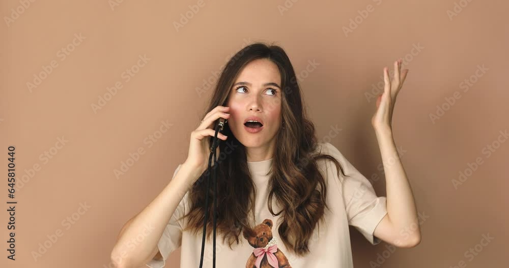 Close up of annoyed irritated young woman with an angry face have call talk looking furious, mad and feeling frustrated isolated on beige background. Brunette curly girl expressions and emotions.