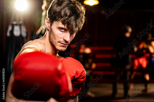 Boxing fighter shirtless posing, caucasian boxer punch his fist in front of camera in aggressive stance and ready to fight at gym with kicking bag and boxing equipment in background. Impetus © Summit Art Creations