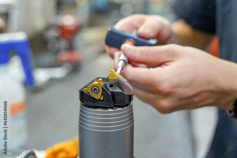 Naklejka premium A worker changes a high speed insert on a milling cutter to work on a CNC milling machine.