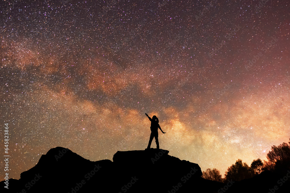 Fantasy landscape, silhouette of a hiker standing on the hill, on the milky way galaxy background.