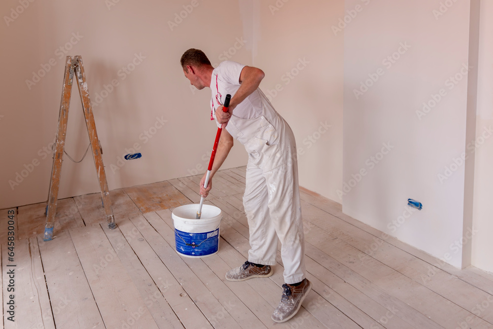 Construction worker painter man with paint roller in his hand and buckets of products to restore and paint the wall, indoor the building site of a house Construction worker painter man with paint roller in his hand and buckets of products to restore and paint the wall, indoor the building site of a house
