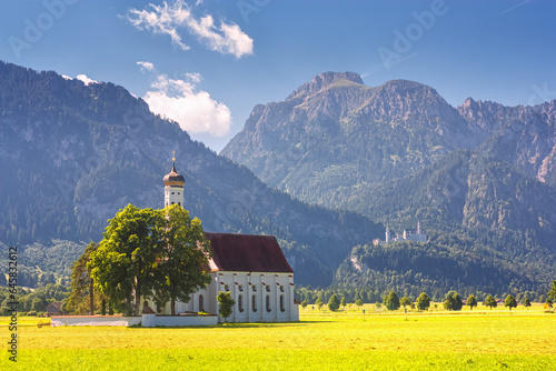 Bavarian landscape - view of the church of St. Coloman on the background of the Alpine mountains and Neuschwanstein Castle in summer day, Germany