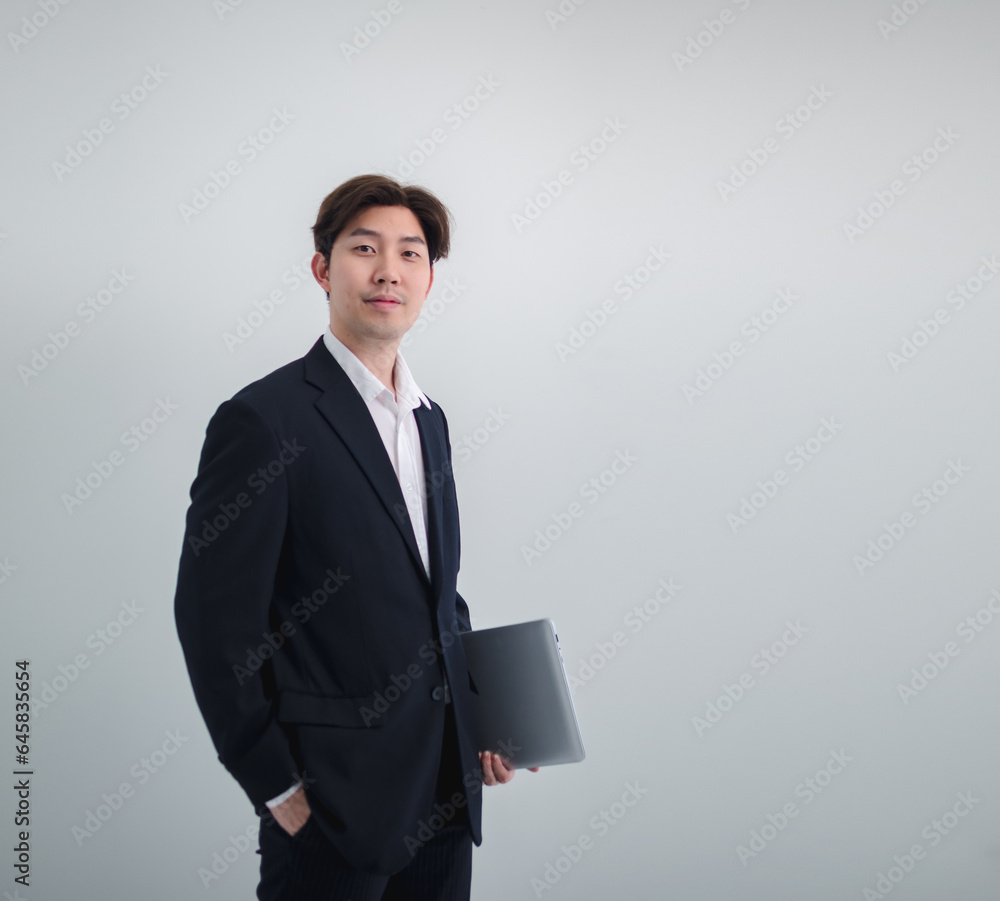 Business man portrait Asian one person wearing a black suit, handsome cool sharp smart standing looking, hand holding mobile phone and laptop ready for work inside the office, with white background Business man portrait Asian one person wearing a black suit, handsome cool sharp smart standing looking, hand holding mobile phone and laptop ready for work inside the office, with white background