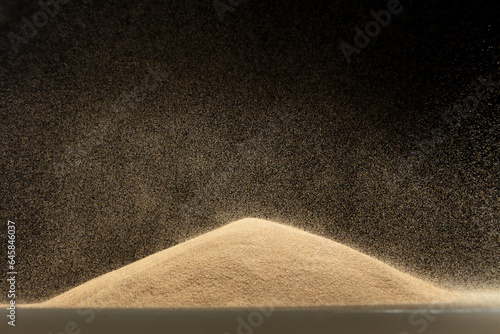Sand fall down on hill like a rain and splash fly in air. Sand dune hill over wind storm and blast dust splash over mountain. Sunshine rain fall on sand hill wind blow. Black background isolated