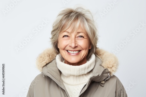 Portrait photography of a French woman in her 60s wearing a warm parka against a white background