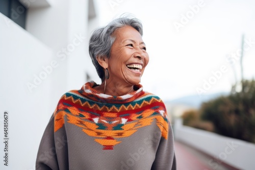 Lifestyle portrait photography of a Peruvian woman in her 70s wearing a cozy sweater against a minimalist or empty room background