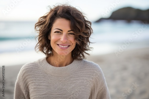 Lifestyle portrait photography of a Italian woman in her 40s wearing a cozy sweater against a beach background © Anne Schaum