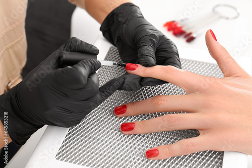 Professional manicurist working with client at white table, closeup