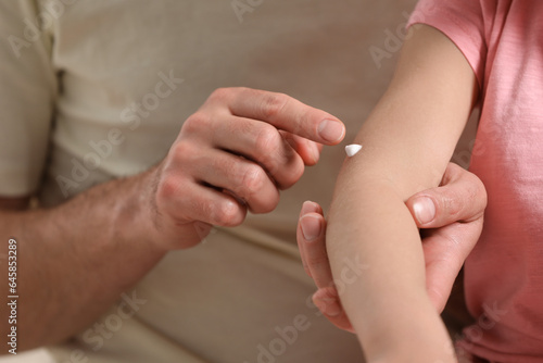 Father applying ointment onto his daughter's arm, closeup