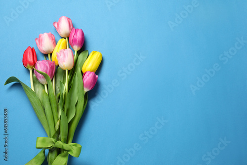 Beautiful colorful tulip flowers and ribbon on light blue background, flat lay. Space for text