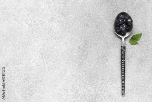Spoon with ripe bilberries and leaves on light grey textured table, top view. Space for text