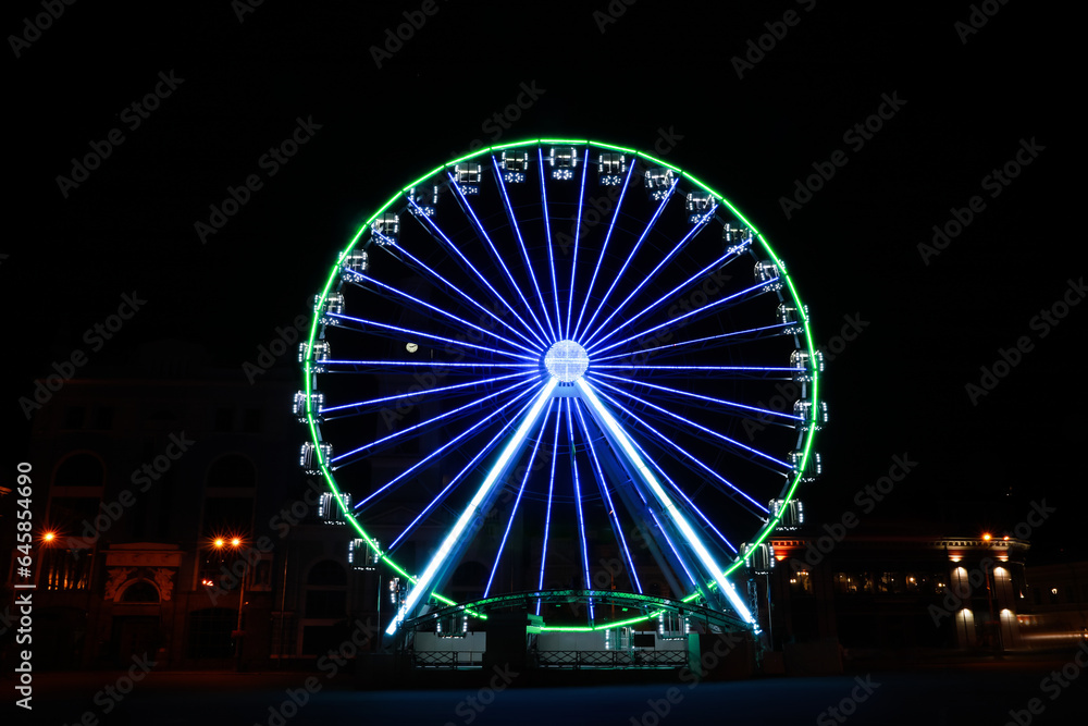 Beautiful glowing Ferris wheel on city street at night