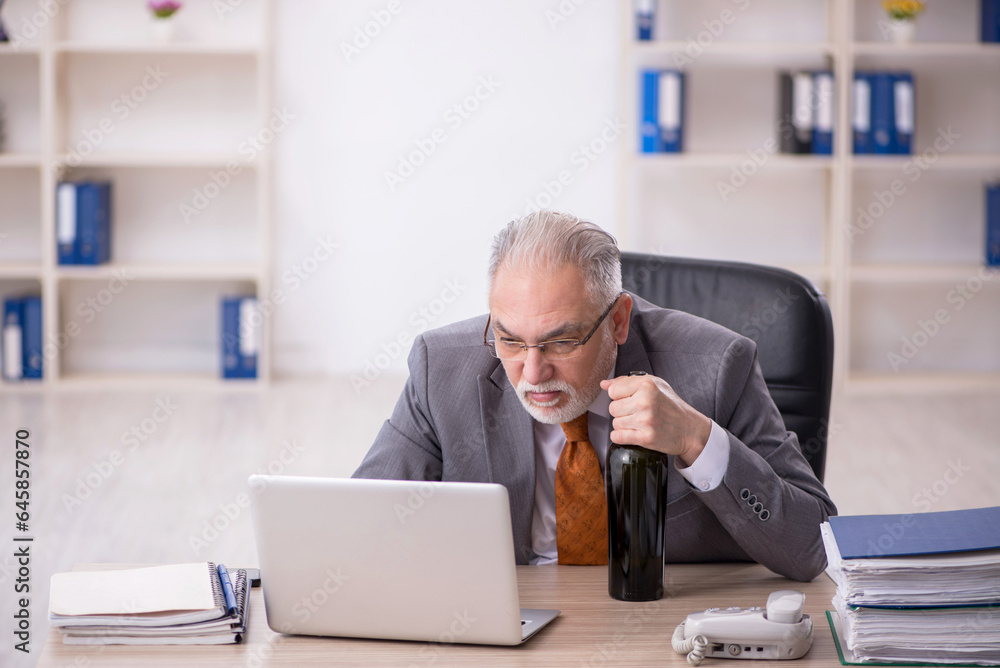 Old male employee drinking alcohol at workplace Old male employee drinking alcohol at workplace