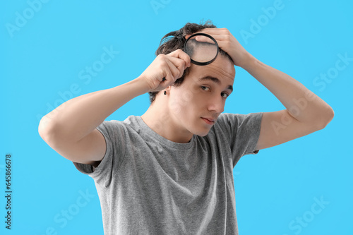 Young man with hair loss problem and magnifier on blue background