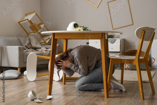 Fényképezés Young woman hiding under dining table during earthquake at home