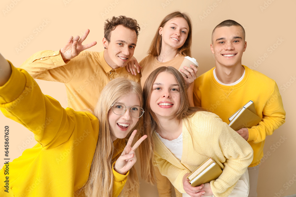 Group of students with books and cup of coffee taking selfie on pale yellow background