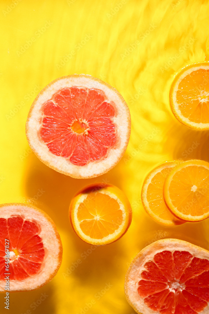 Slices of fresh orange and grapefruit in water on yellow background Slices of fresh orange and grapefruit in water on yellow background