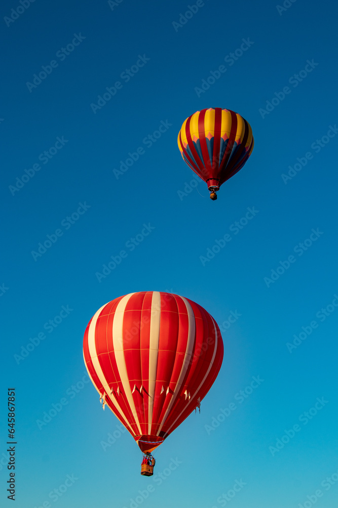 Two red and yellow Hot Air Balloons soaring against a bright blue sky
