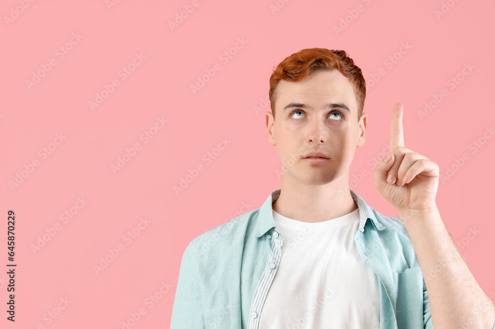 Naklejka premium Thoughtful young redhead man pointing at something on pink background