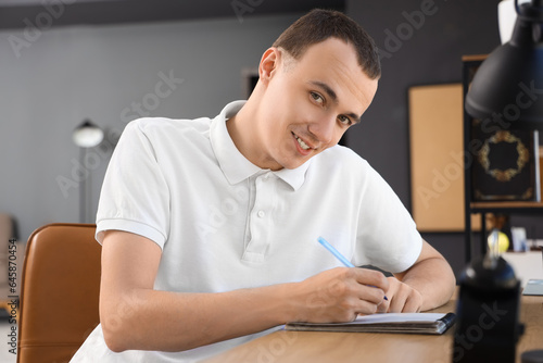 Young man writing at table ...