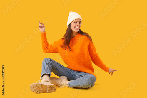 Young woman in winter clothes sitting on yellow background © Pixel-Shot