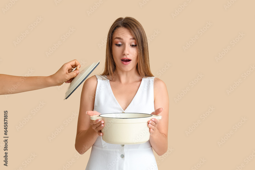 Surprised young woman with cooking pot of chicken soup on beige background Surprised young woman with cooking pot of chicken soup on beige background