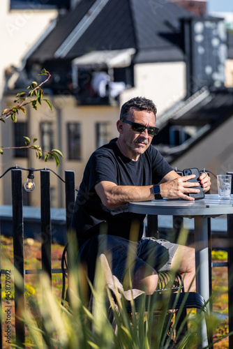 Photography Stockholm, Sweden  A man with sunglasses sits at a rooftop bar in the sun holding a phone