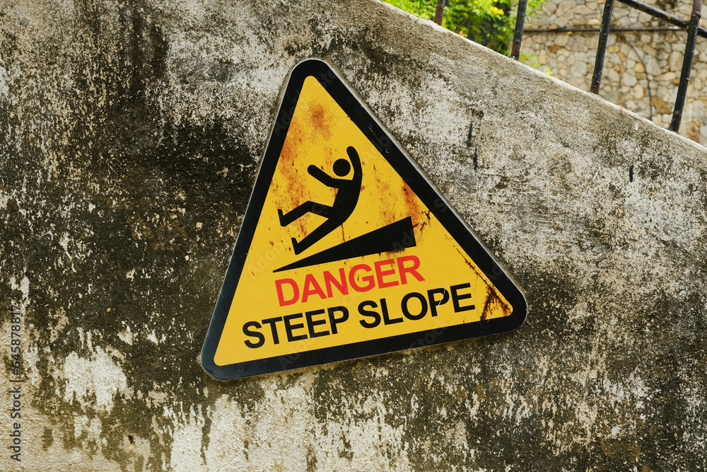 A picture of warning sign of danger steep slope at the wall. A picture of warning sign of danger steep slope at the wall.