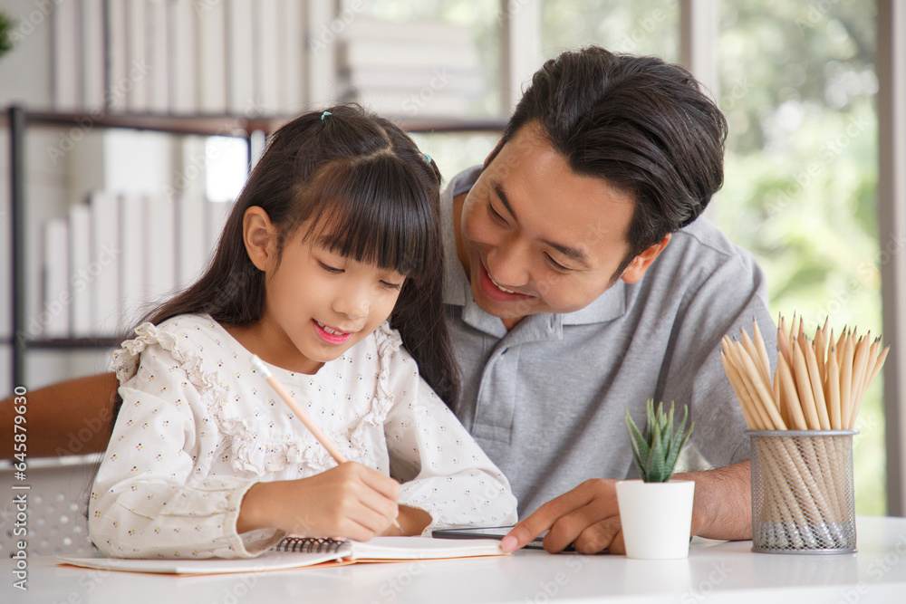 Children education and home school concept : Young asisn father pleased to see little daughters' study success. Excited smiling small child girl enjoying learning and writing with pleasant dad at home Children education and home school concept : Young asisn father pleased to see little daughters' study success. Excited smiling small child girl enjoying learning and writing with pleasant dad at home