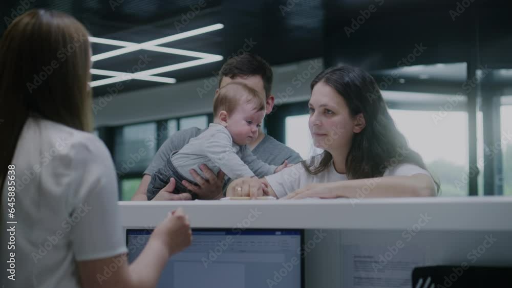 Family with little child stand near reception desk in clinic lobby. Woman fills out papers, makes appointment with doctor, talks with female administrator. Medical staff work in modern medical center. Family with little child stand near reception desk in clinic lobby. Woman fills out papers, makes appointment with doctor, talks with female administrator. Medical staff work in modern medical center.