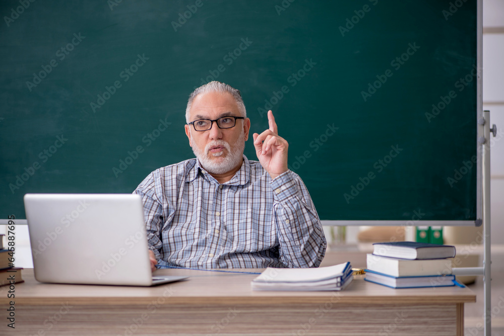 Old male teacher sitting in front of green board Old male teacher sitting in front of green board