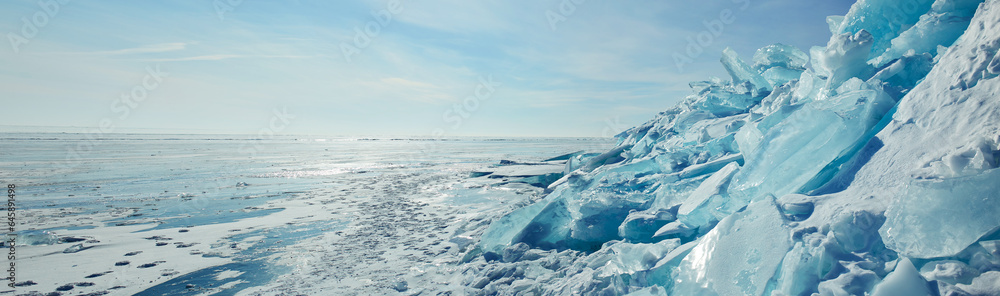 Huge blocks of transparent blue ice, hummocks on the frozen Lake Baikal. Winter landscape, panorama