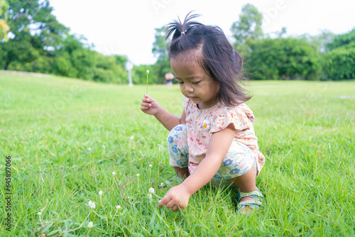 Adorable little child girl playing on green meadow grass outdoor city park