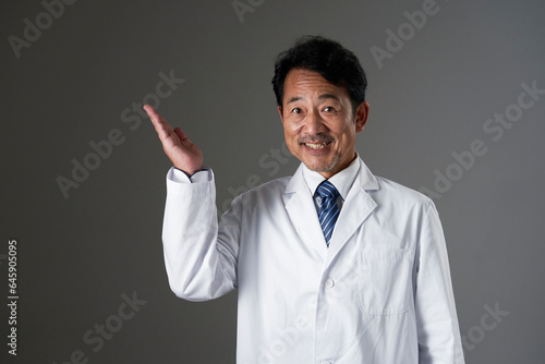左側を手の平で指す中年の医師　黒背景 © siro46