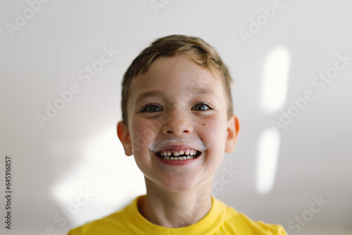 Cute boy drinks kefir or milk. Funny portrait of a boy with a milk mustache. Lifestyle
