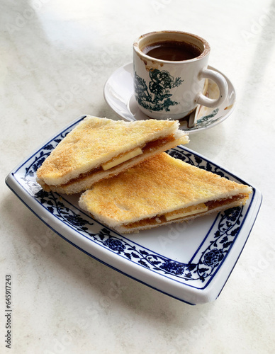 local Malaysia Singapore baked kaya jam butter toast bun white bread in plate and nanyang hot kopi coffee in traditional flower cup on white table asian cuisine halal food restaurant banquet cafe menu