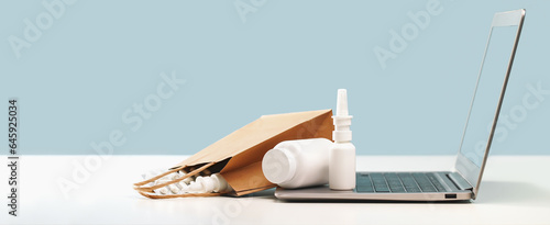 Online pharmacy. prescription drugs and over the counter medication ready for delivery to customers. Pills and spray white mockup containers and buff paper bags over the laptop. Drugstore shopping