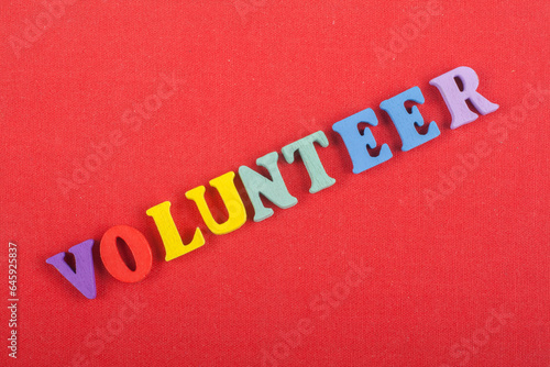 VOLUNTEER word on red background composed from colorful abc alphabet block wooden letters, copy space for ad text. Learning english concept.
